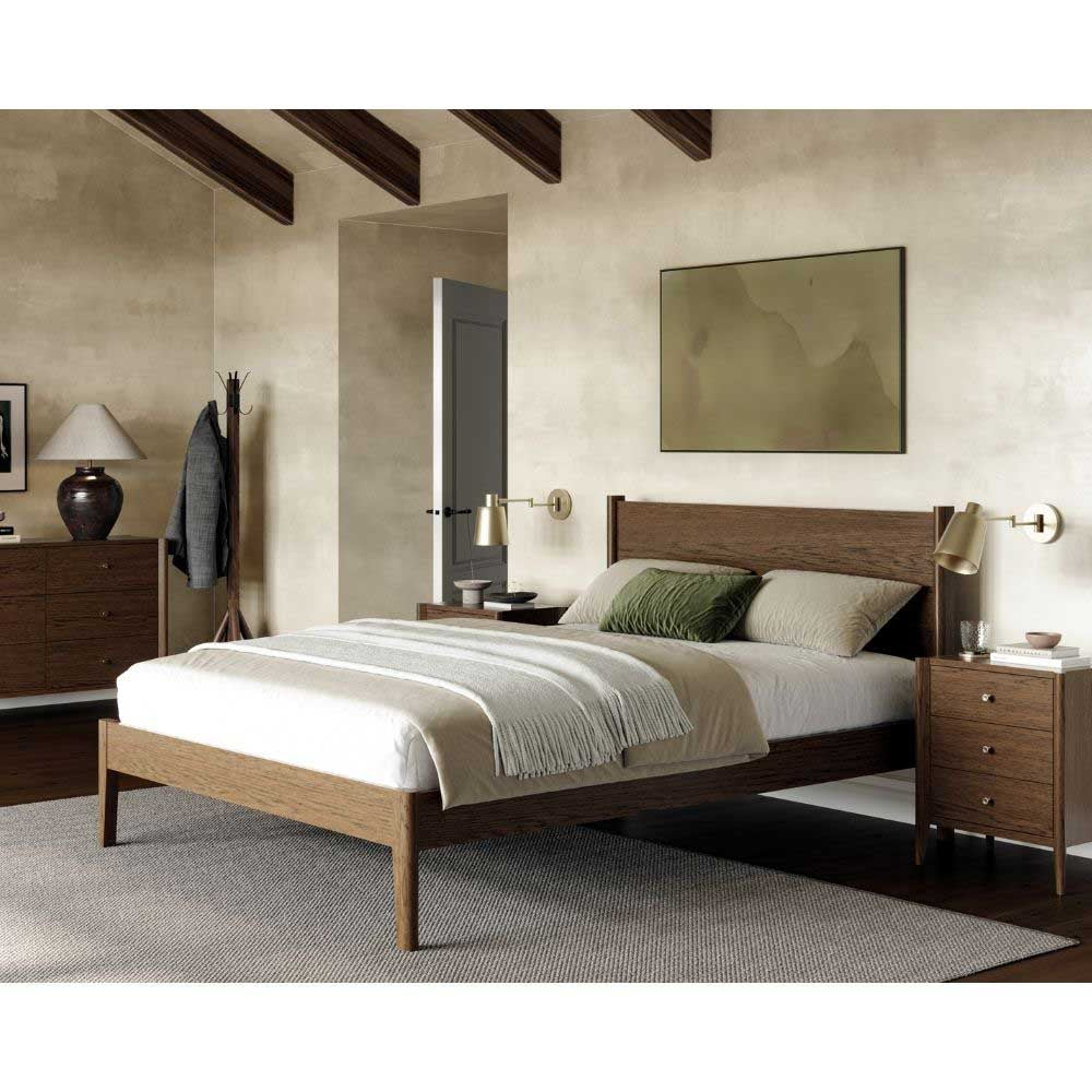 A modern wooden bed frame with a low-profile platform base and a tall rectangular headboard, styled in a bedroom setting with white and green bedding, matching nightstands, and wall-mounted lamps.