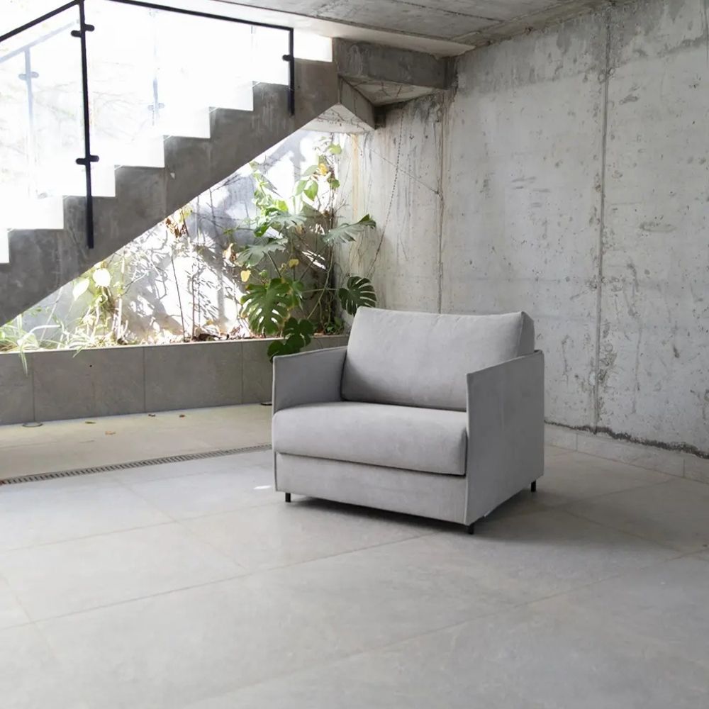 Gray sofa bed in a modern room with concrete walls and stairs