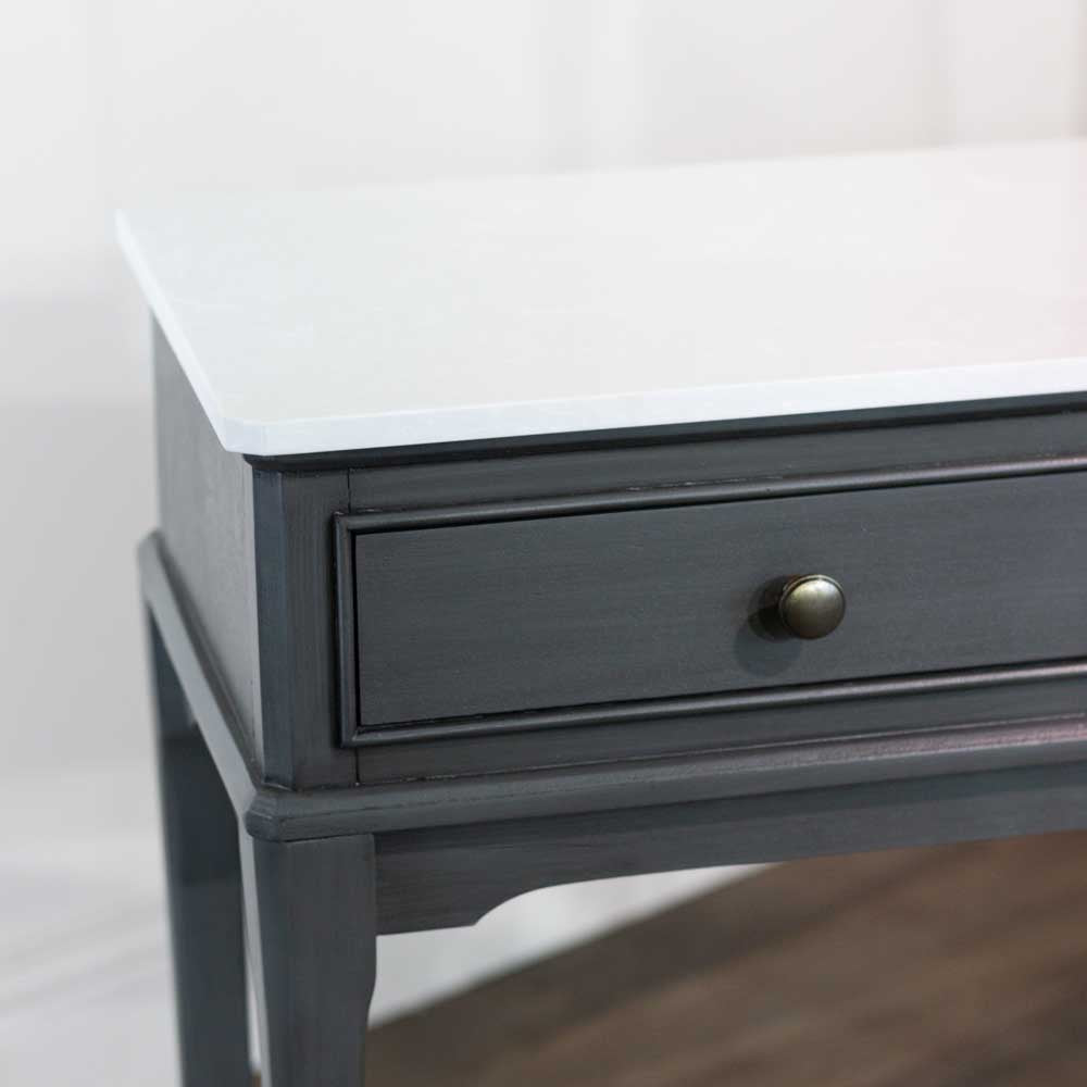 Close-up of a dark brown / grey wooden console table with a white marble top and a single round metallic drawer knob.