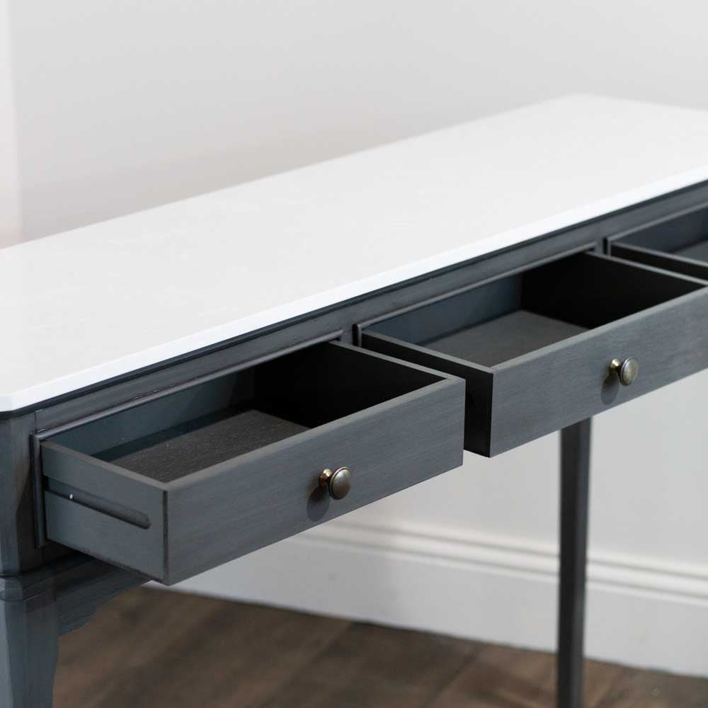 A dark brown / grey console table with a white top surface, featuring two open drawers with round metallic knobs, shown in a home interior setting.