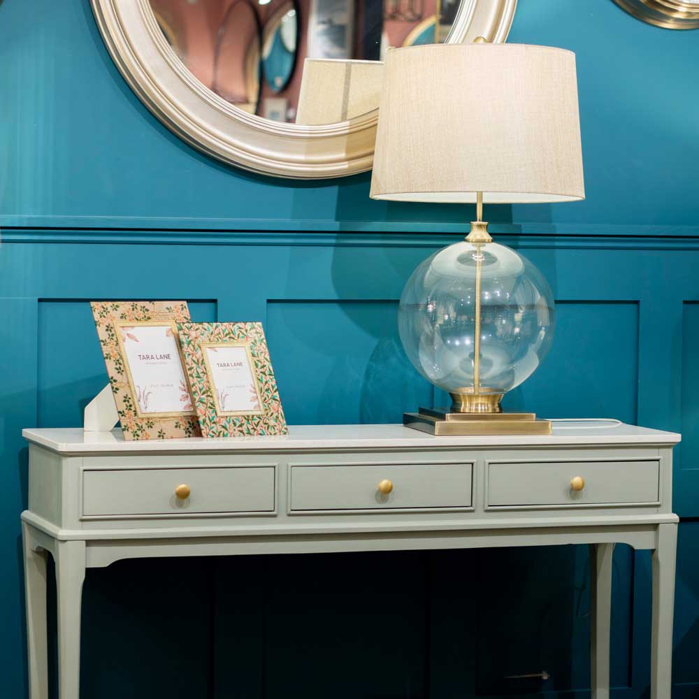 Close up of Sage green console table with a lamp and picture frames against a blue wall
