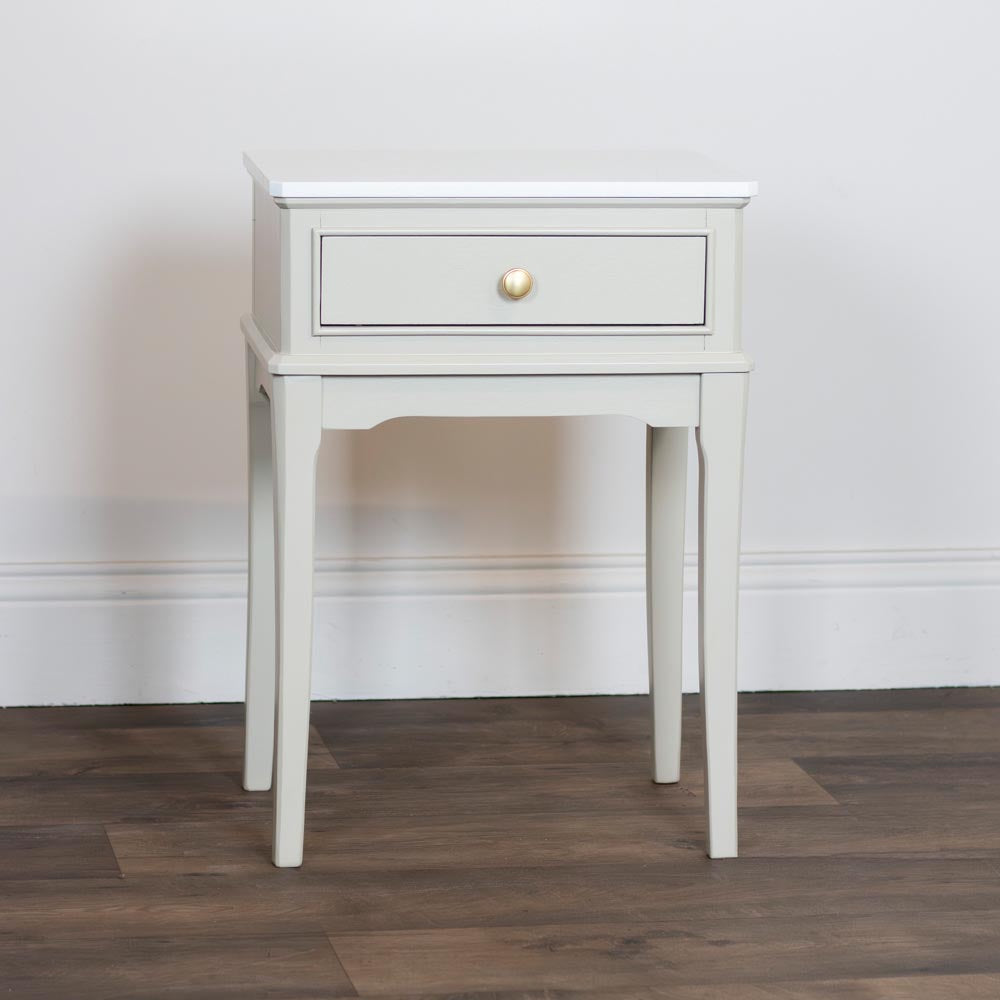 Taupe / beige nightstand with a single drawer on a wooden floor against a white wall