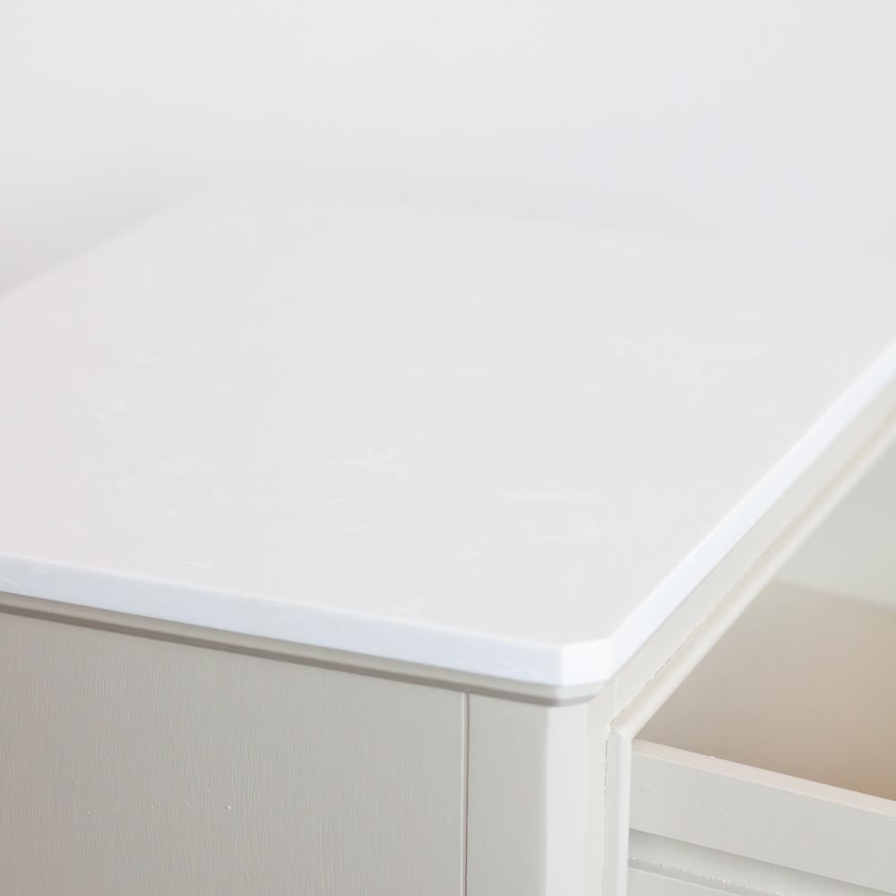 Close-up of a stone coloured wooden drawer with a smooth white marble top surface and a partially open drawer on the right.
