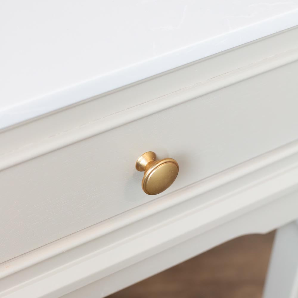 A close-up of a stone coloured wooden drawer with a round, brushed gold metal knob.