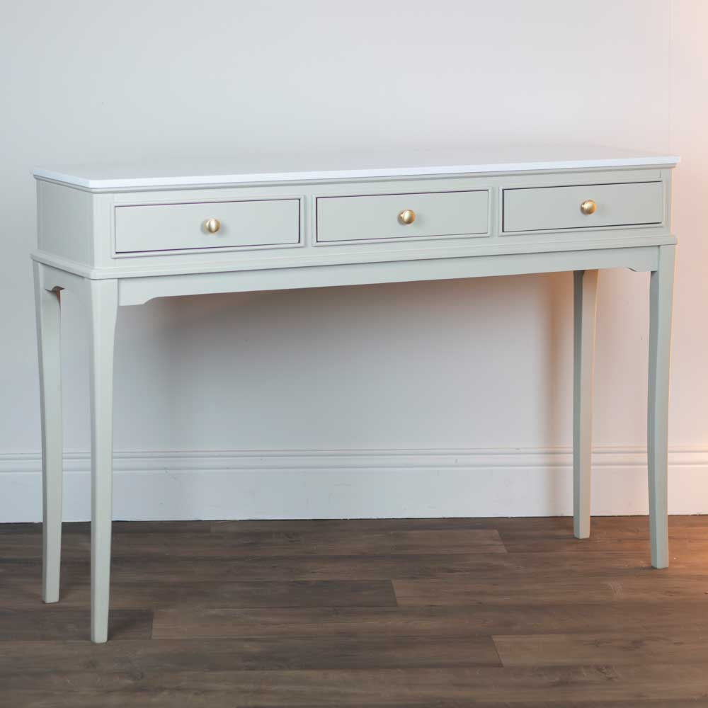 Light beige / stone coloured console table with three drawers on a wooden floor against a white wall