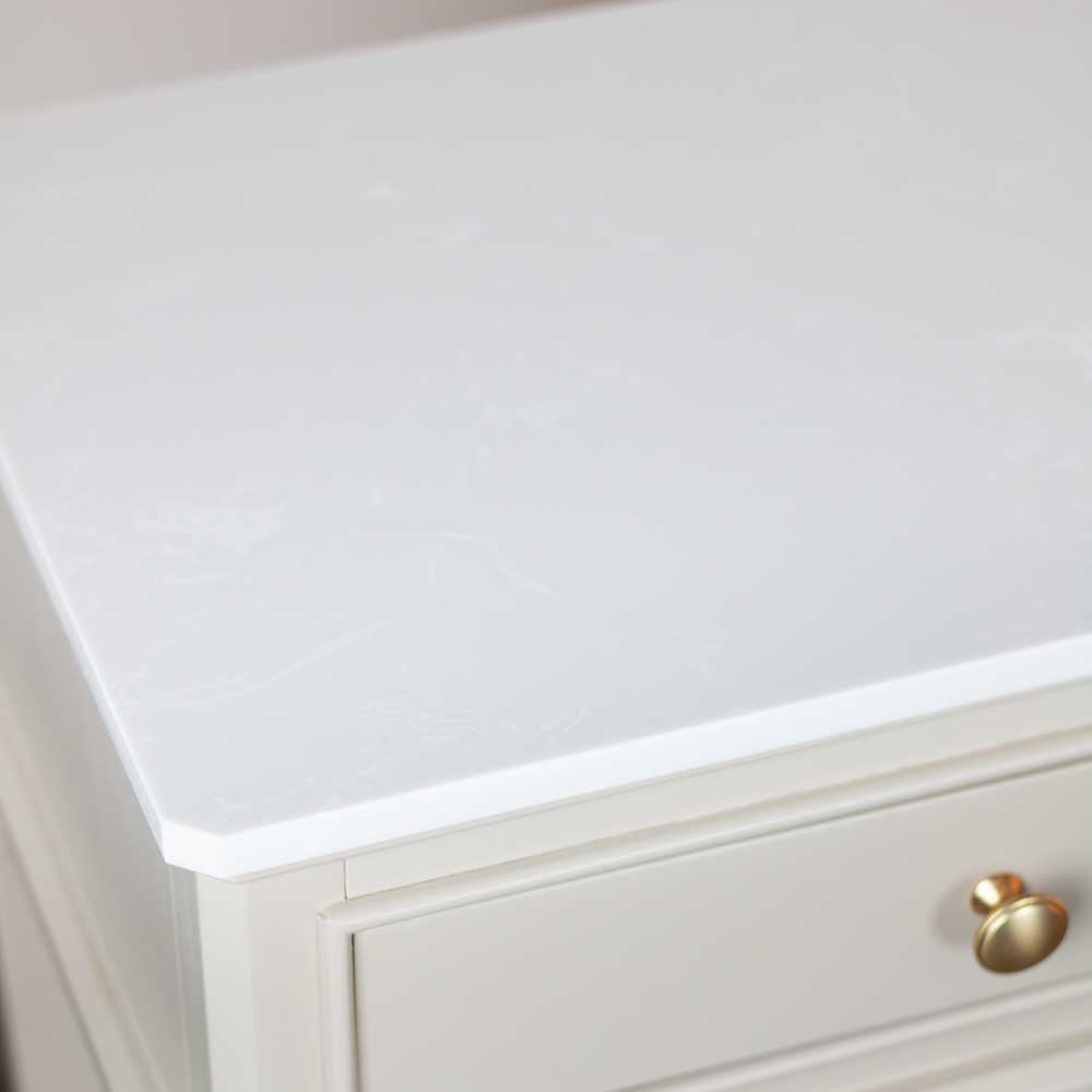 A close-up of a beige / stone coloured drawer with a gold round knob, set against a white marble top.