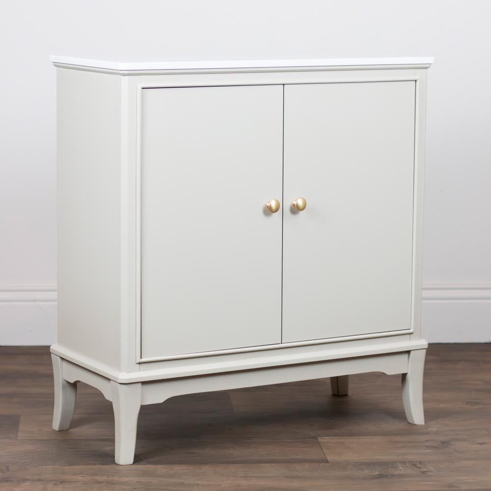 A small Stone / taupe / beige cabinet with two doors and round gold knobs, shown on a wood floor against a white wall.