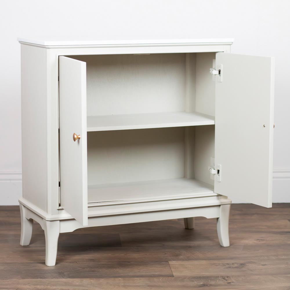A Stone / taupe / beige two-door cabinet with an open front, featuring a single shelf inside and small curved legs, shown on a wood floor against a white wall.