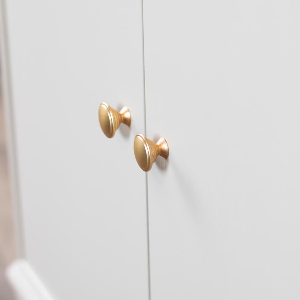 Two round brushed brass cabinet knobs mounted on Stone / taupe / beige cabinet doors.