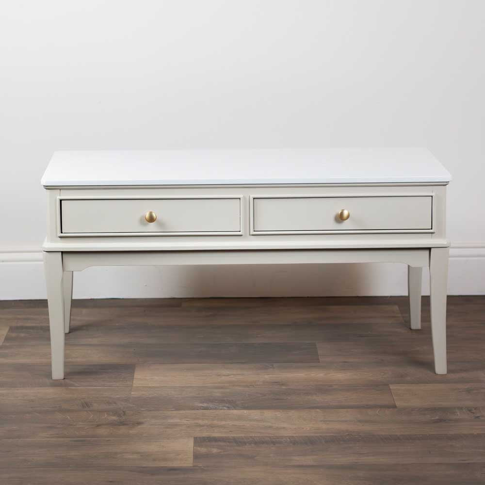 A light beige / stone coloured coffee table with two drawers on a wooden floor against a white wall