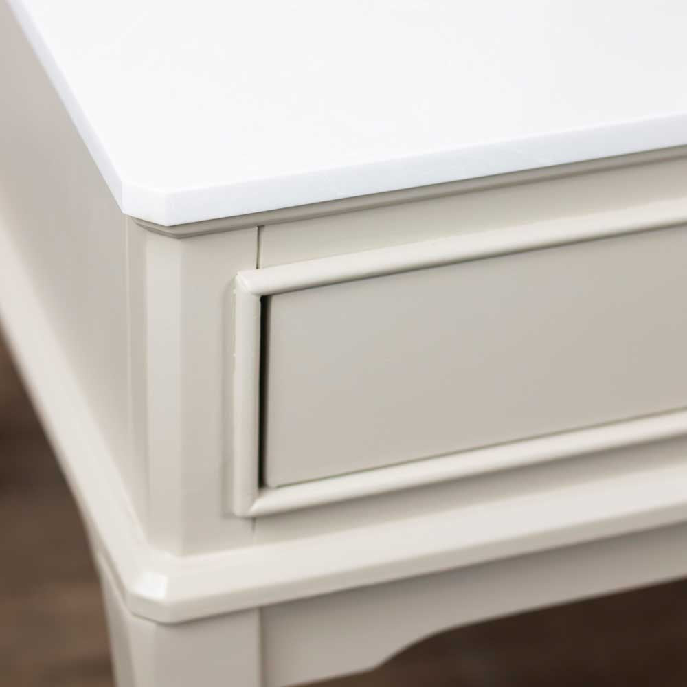 Close-up of a A light beige / stone coloured wooden coffee table showing the marble corner of the top and a drawer front with decorative molding.