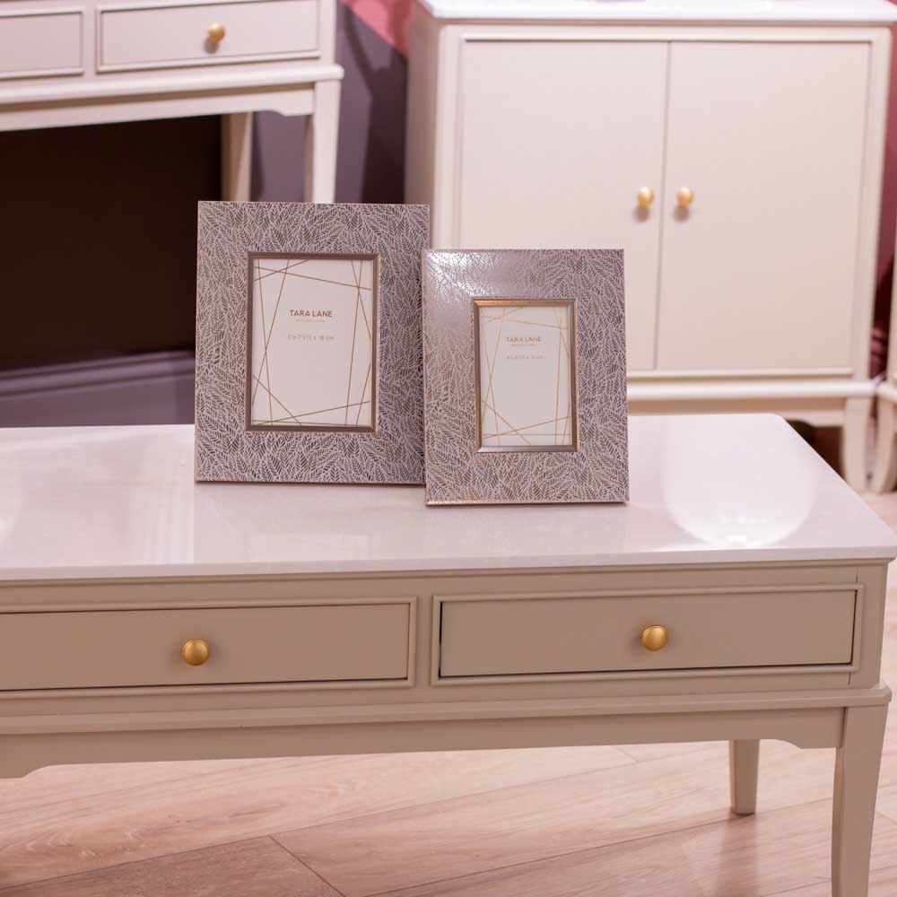 Two decorative picture frames with a textured gray and white patterned border, displayed on a light beige / stone coloured coffee table in a living room setting.