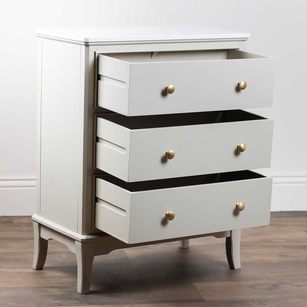 Beige / stone coloured dresser with gold knobs on a wooden floor and white wall background