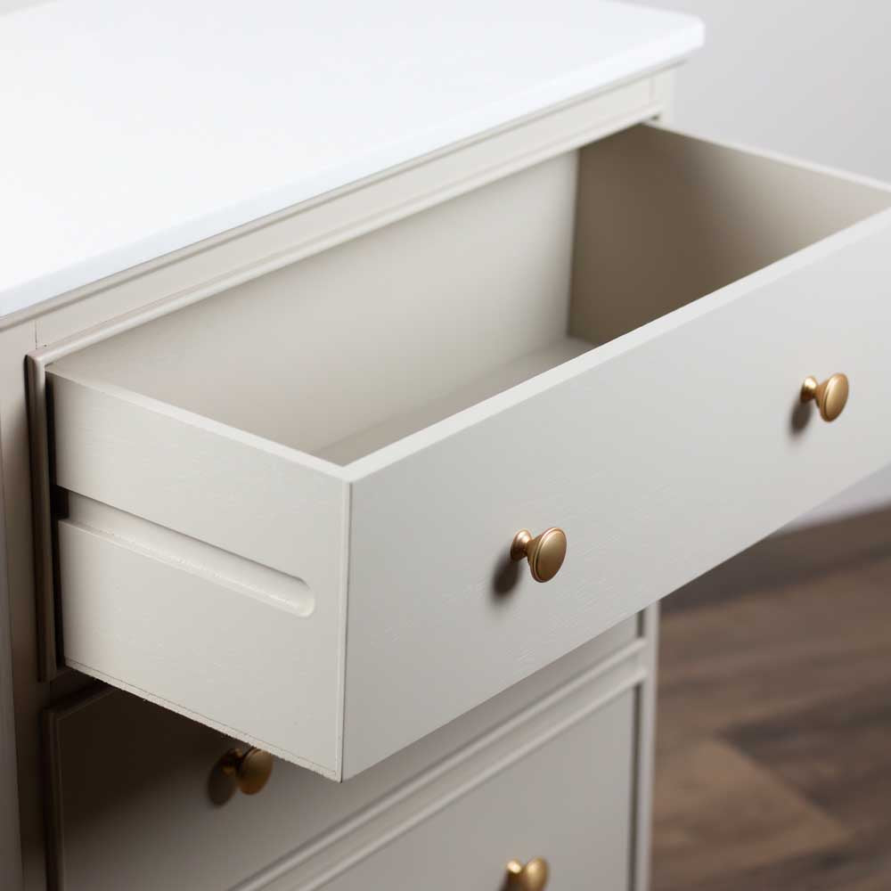 Open drawer of a light beige / stone coloured chest of drawers with brushed brass knobs on a neutral background