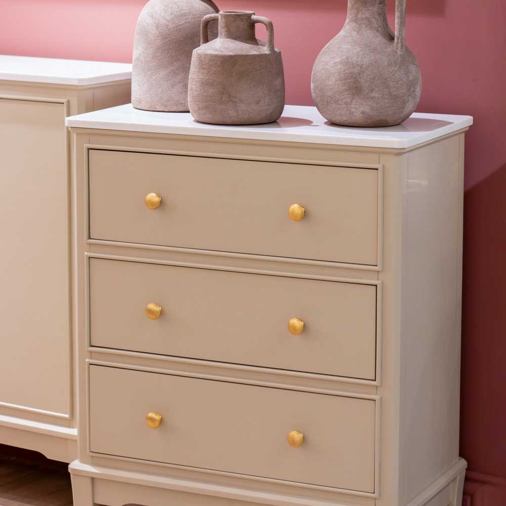 Beige / stone coloured dresser / chest of drawers with gold knobs against a pink wall