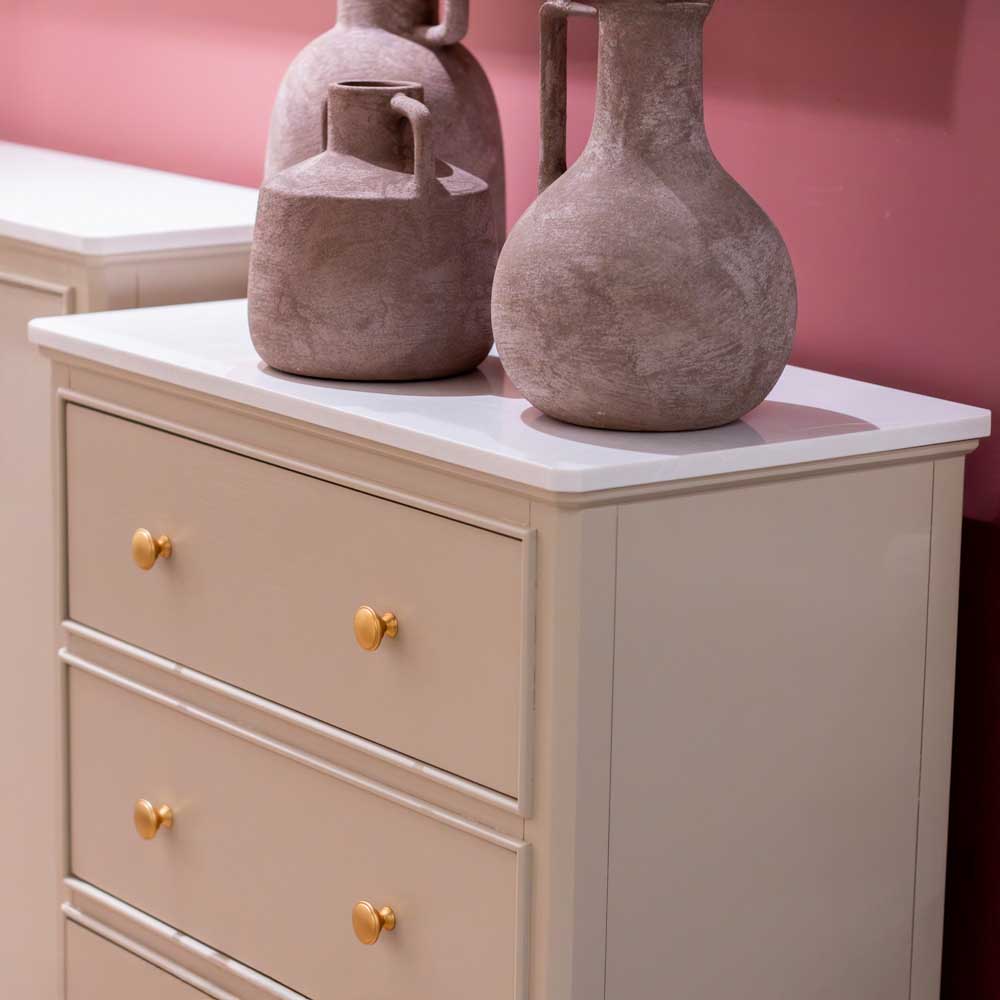 Two ceramic vases on a beige / stone coloured dresser with gold knobs against a pink wall.