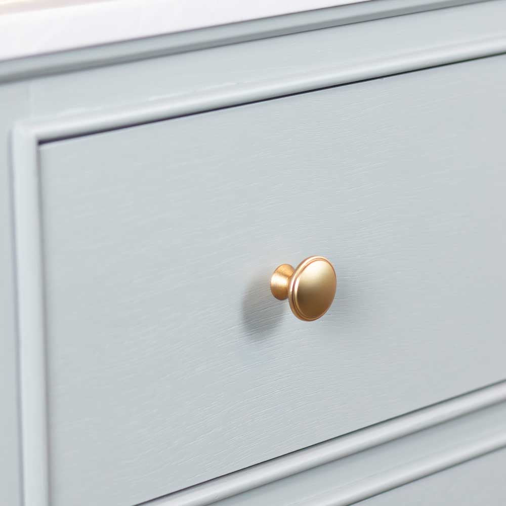 A close-up of a sage green wooden cabinet drawer featuring a round, polished gold pull knob.