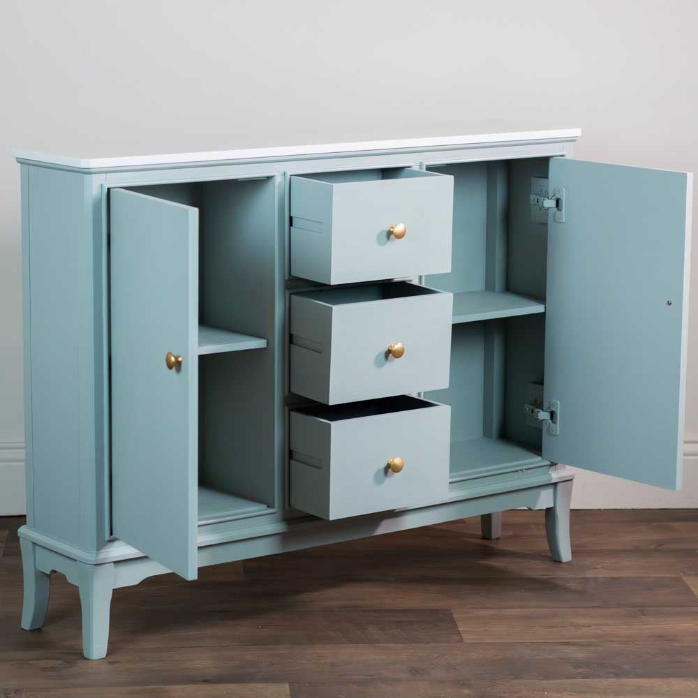 A sage green painted wooden sideboard cabinet with three drawers and two open doors, shown on a dark wood floor against a plain light wall.
