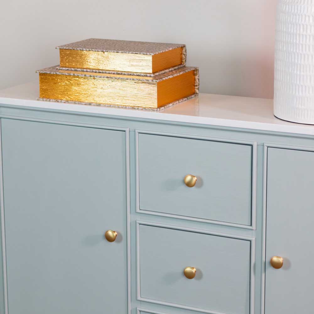 Sage green sideboard cabinet with gold knobs and decorative boxes on top