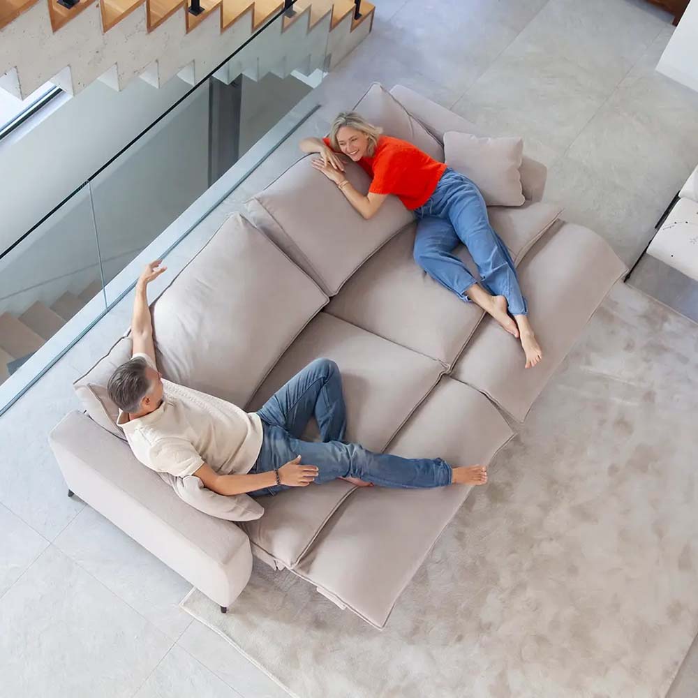 Two people lying on a large beige sectional sofa in a modern living room.