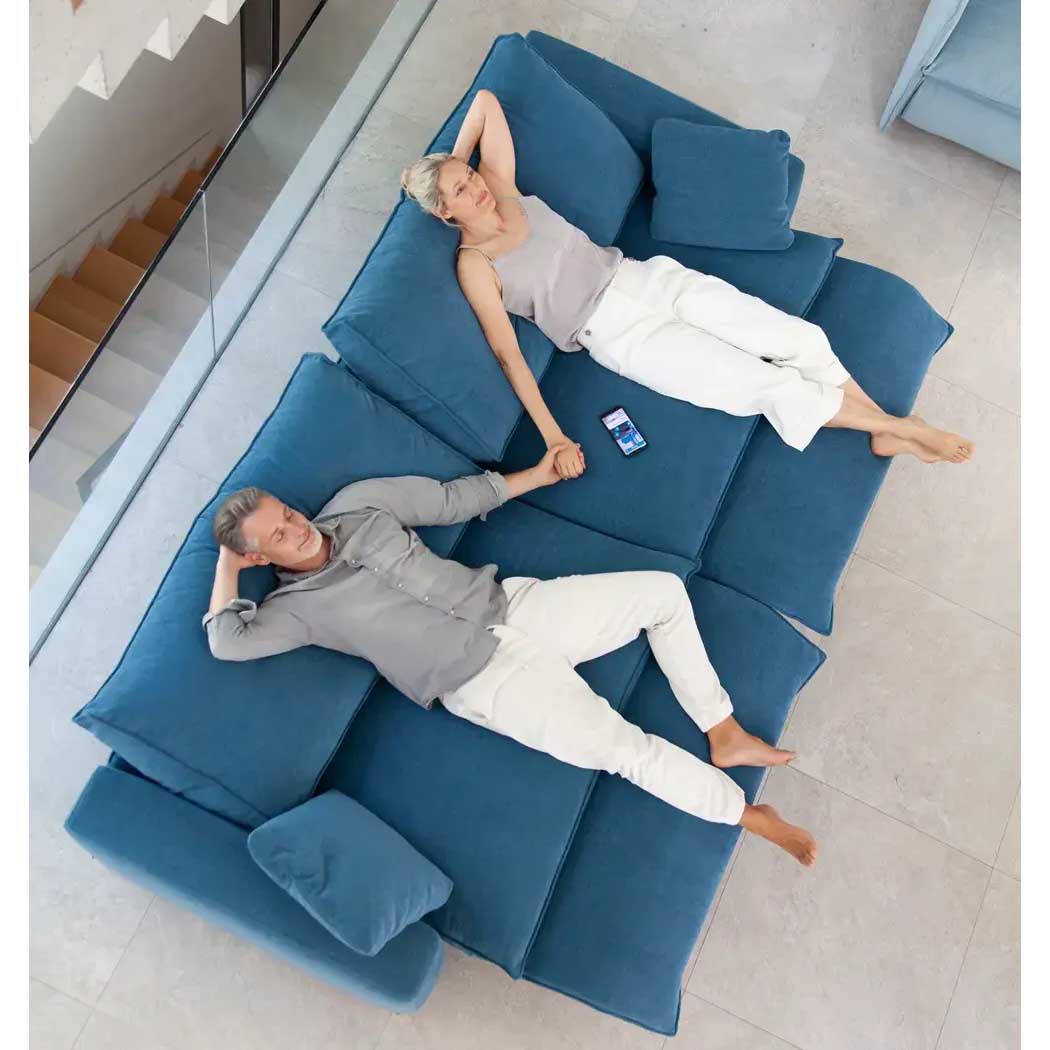 Two people lying on a blue sectional sofa in a modern living room.