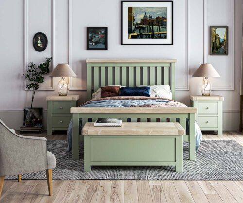 Lifestyle photo of sage bed complete with bedding in bedroom with matching sage bedside locker, and blanket box/ There are photos on the wall and a lamp on the bedside table.