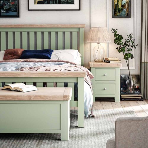 Lifestyle photo of sage bed in bedroom with matching sage bedside locker, and blanket box/ There are photos on the wall and a lamp on the bedside table.